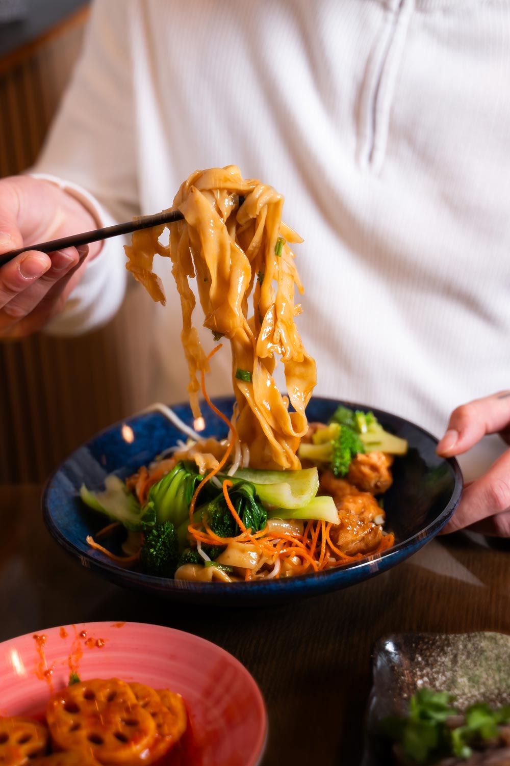 Eine Person in weißem Oberteil isst Nudeln mit Stäbchen aus blauer Schüssel