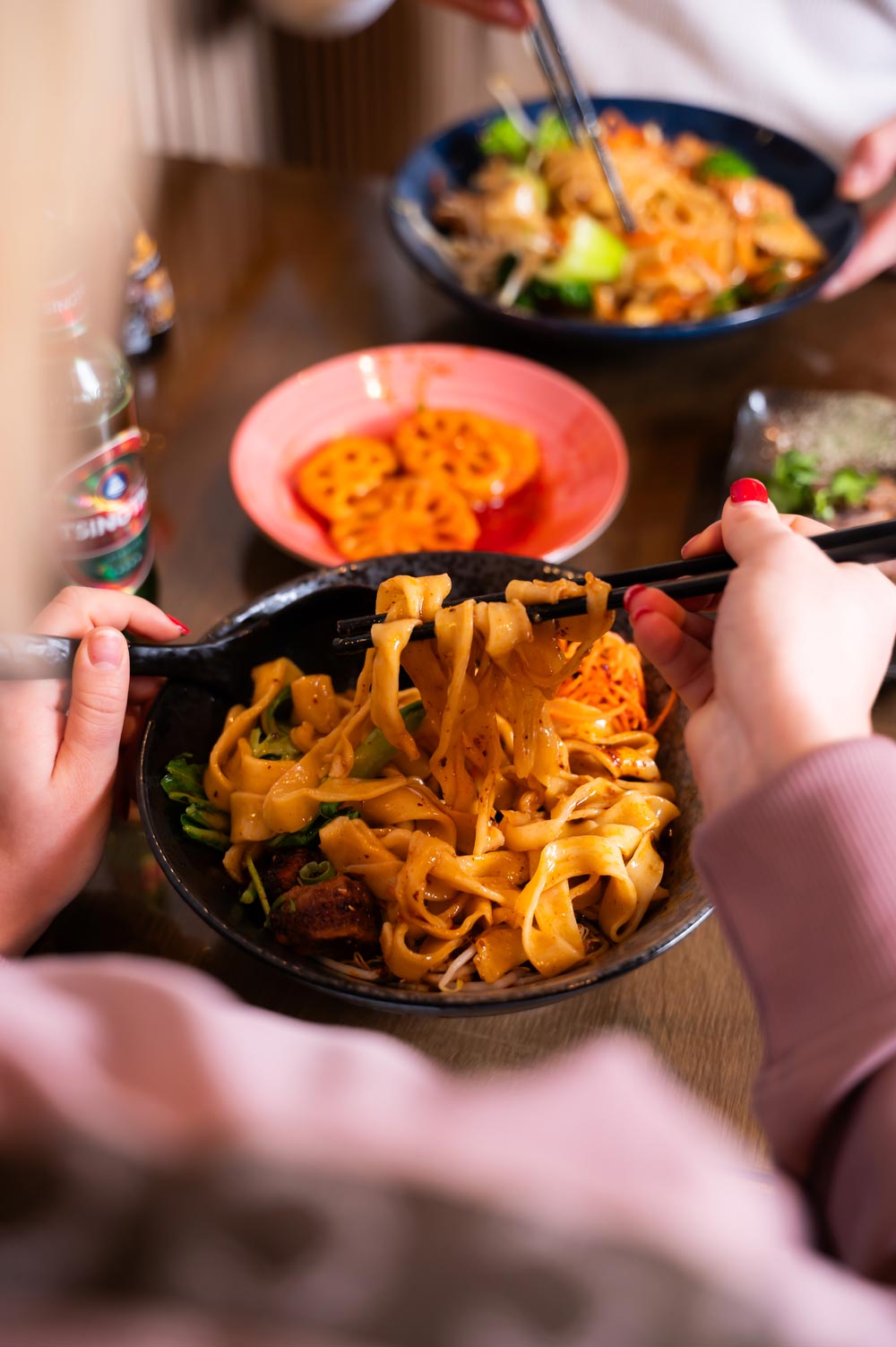 Eine Person isst mit Stäbchen Nudeln aus einer schwarzen Schüssel.