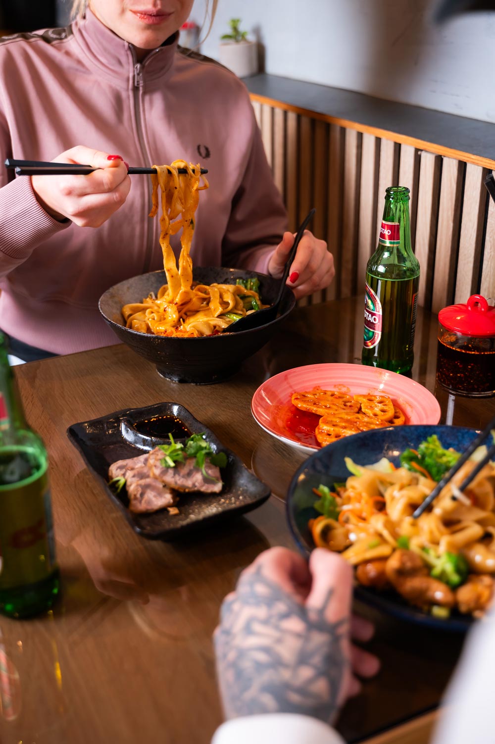Eine Frau in einer rosa Jacke genießt Nudeln mit Stäbchen in einem Restaurant.